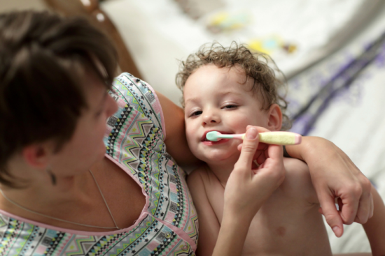 Une femme tient un jeune enfant dans ses bras et lui brosse les dents