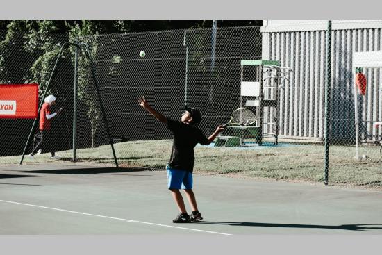 un enfant sur un court de tennis en train de servir